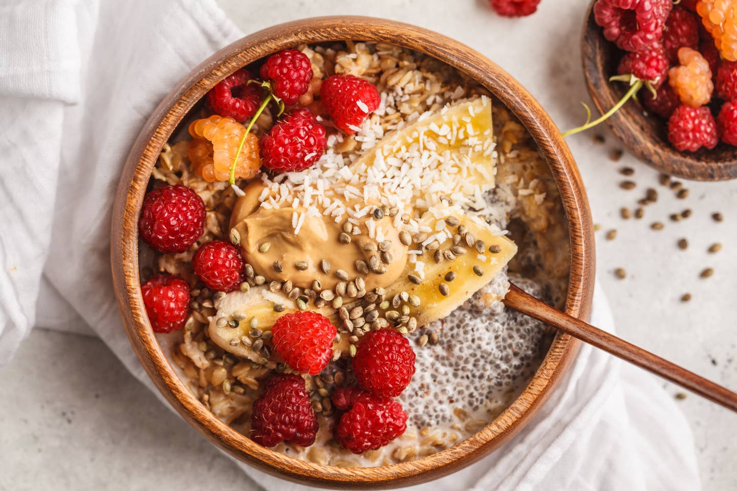 Oatmeal porridge with chia seeds, berries, peanut butter and hemp seeds in wooden bowl, white background.