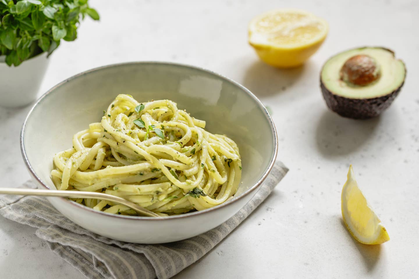 Pasta with avocado and Greek basil sauce in a ceramic bowl on a white table.