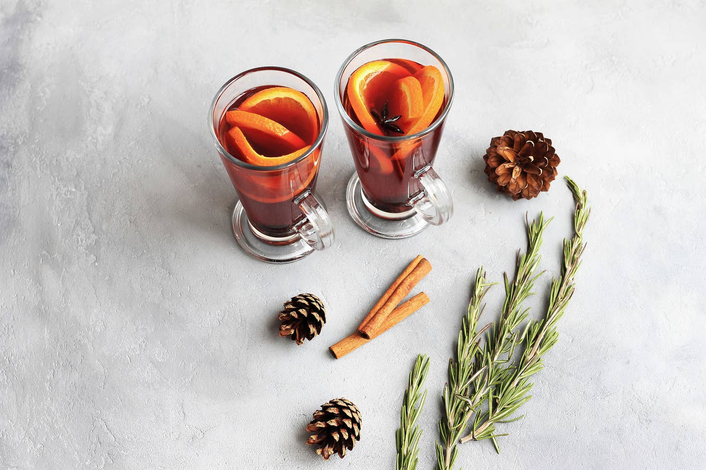 Two glasses of hot red mulled wine or gluhwein with orange, cinnamon sticks on light background. Spicy warm beverage. Seasonal mulled drink.