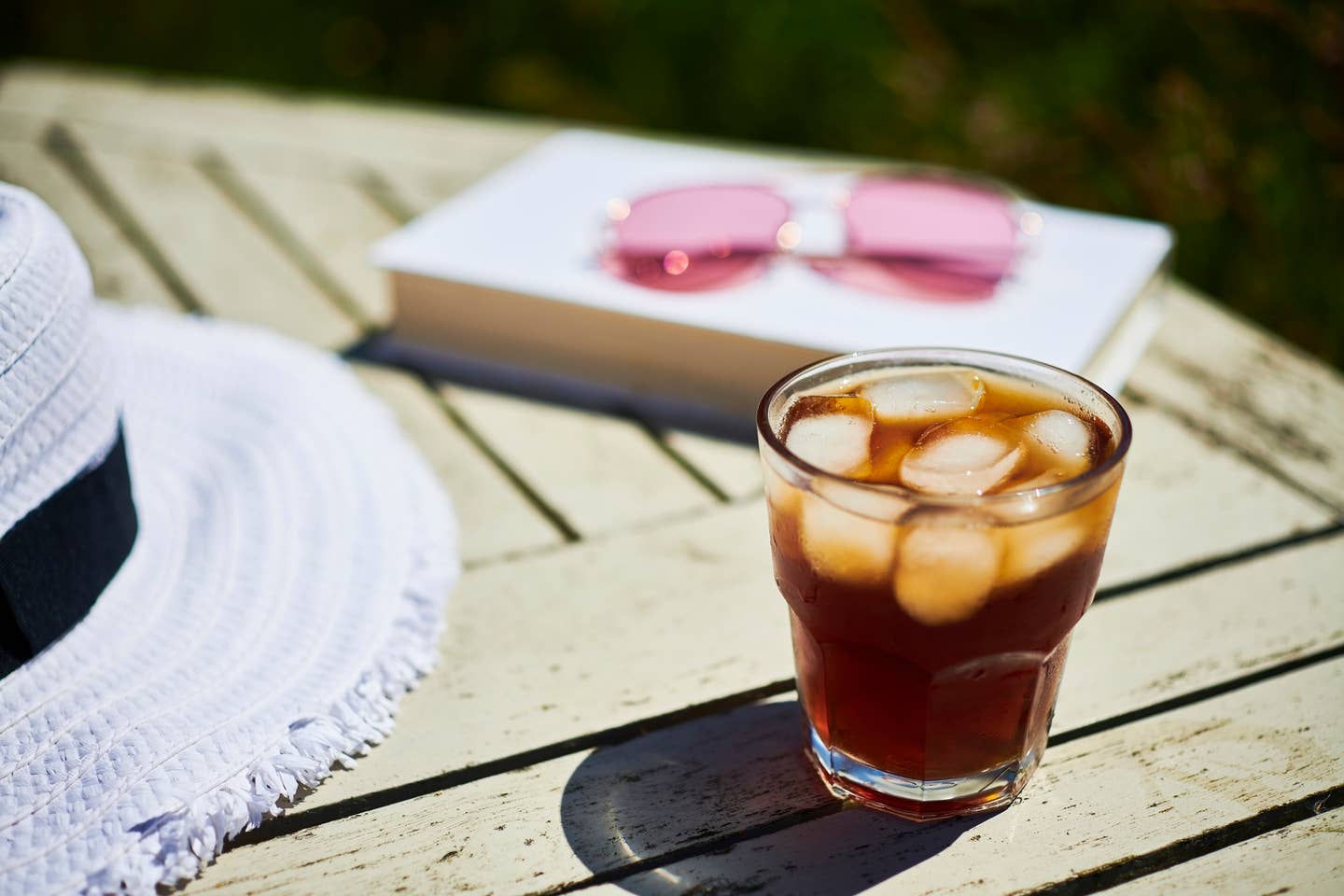 Summer Garden scene, Glass of black Iced Coffee on a garden table in bright sunshine.