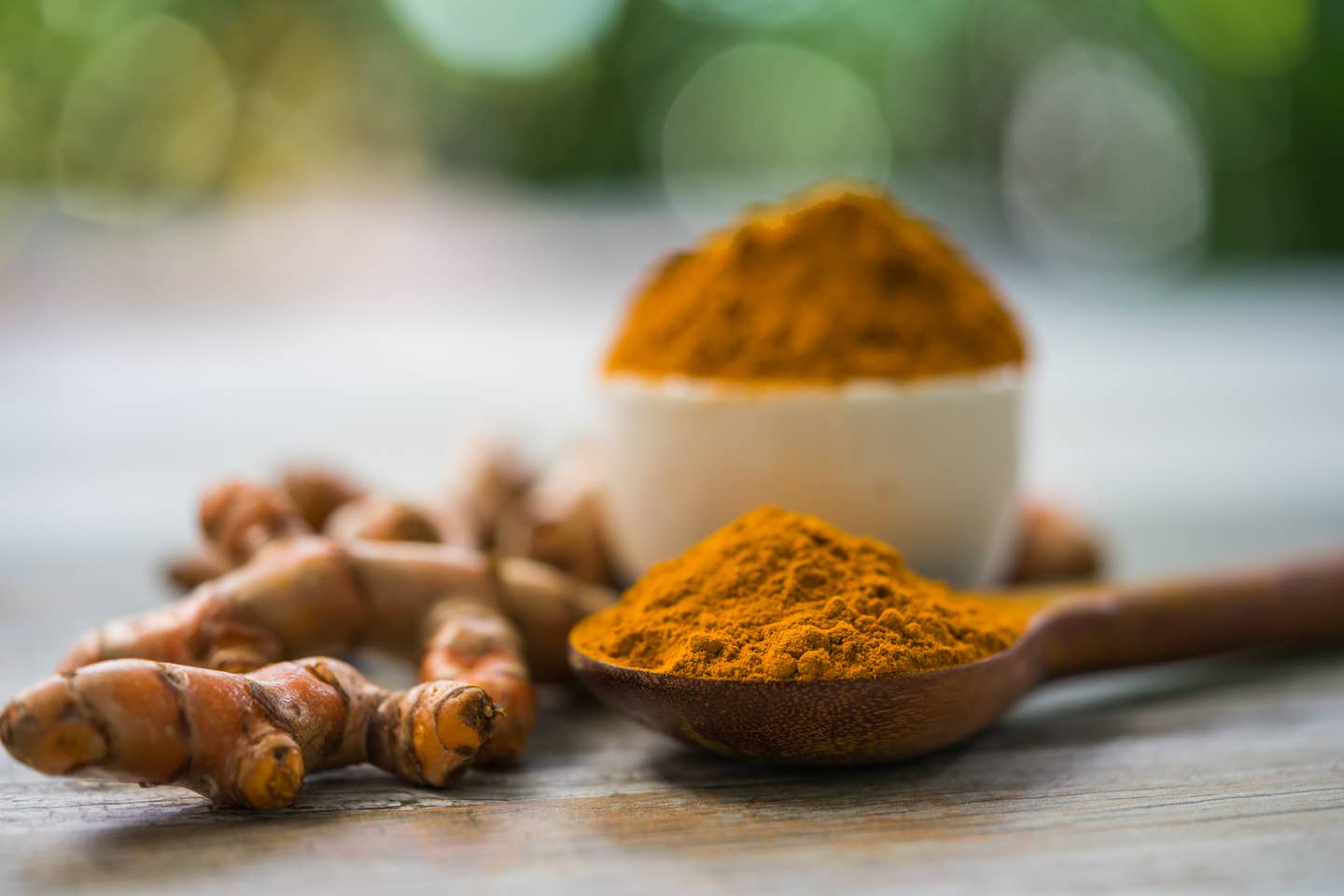 Turmeric powder and fresh turmeric in wood bowls on wooden table.