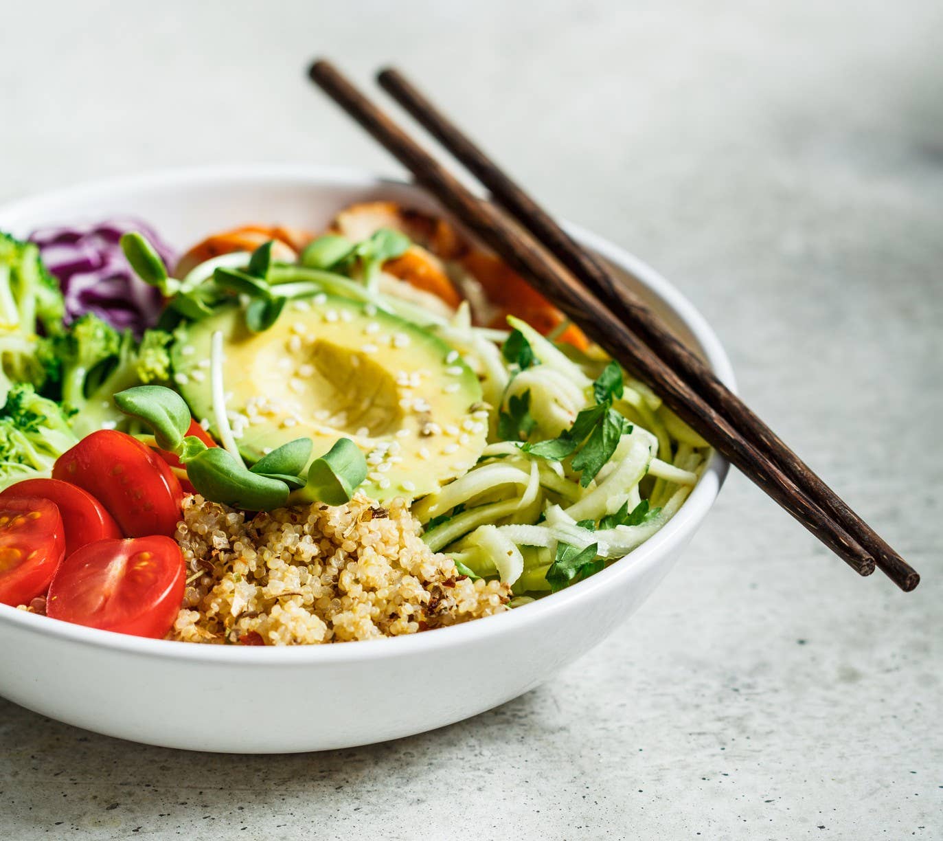 Quinoa salad with broccoli, tomatoes and avocado in white bowl.