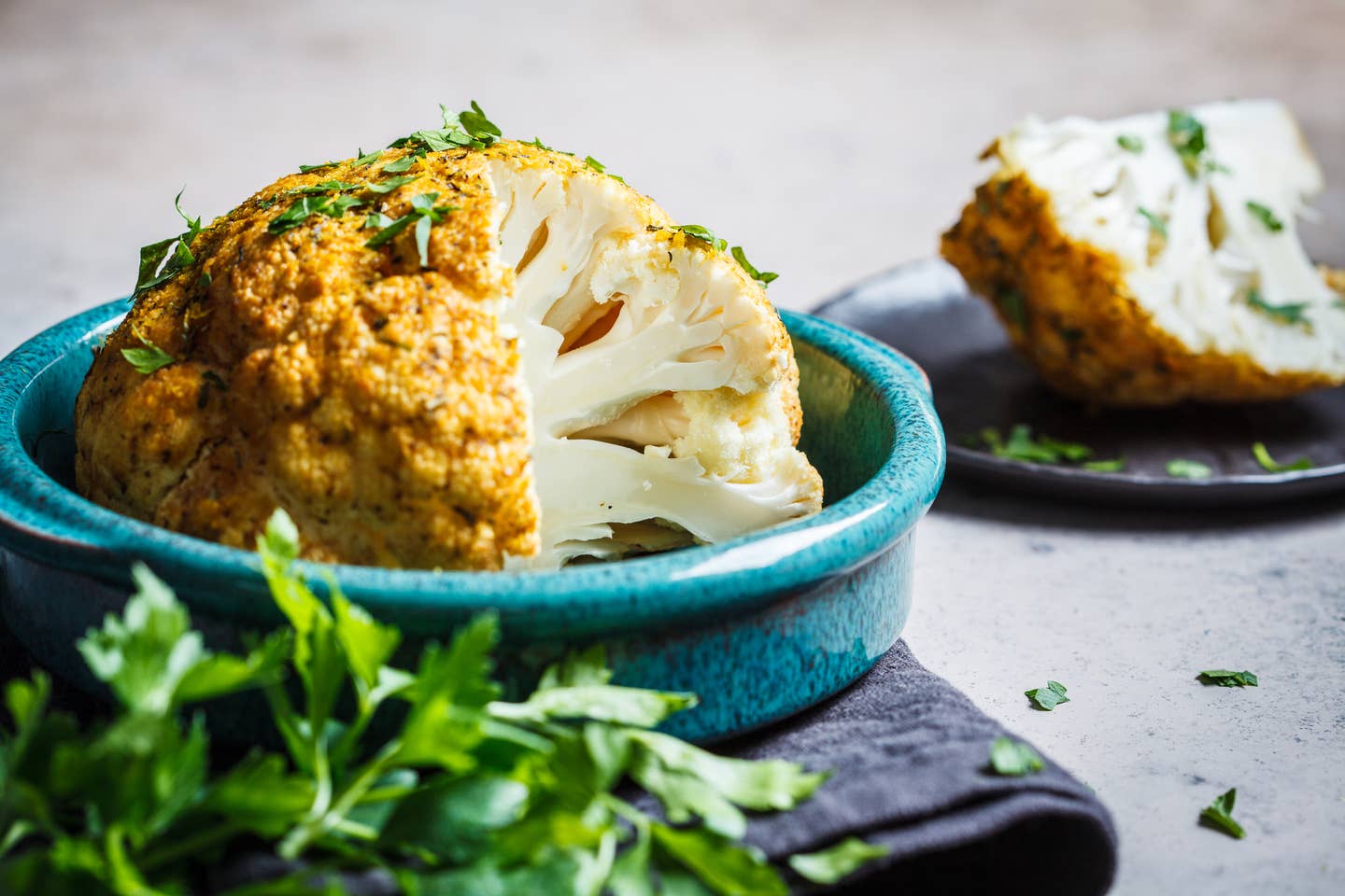 Whole baked cauliflower with spices and herbs in blue dish.