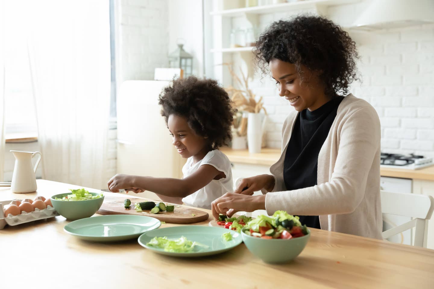 Smiling young african ethnicity woman cooking with small daughter.