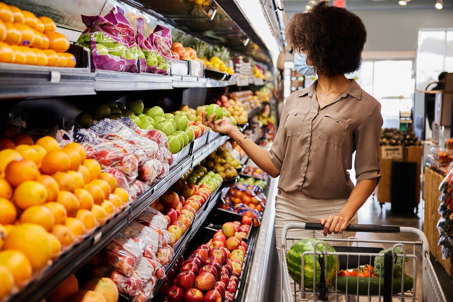 Young woman in a face mask looking at fruit in a supermarket