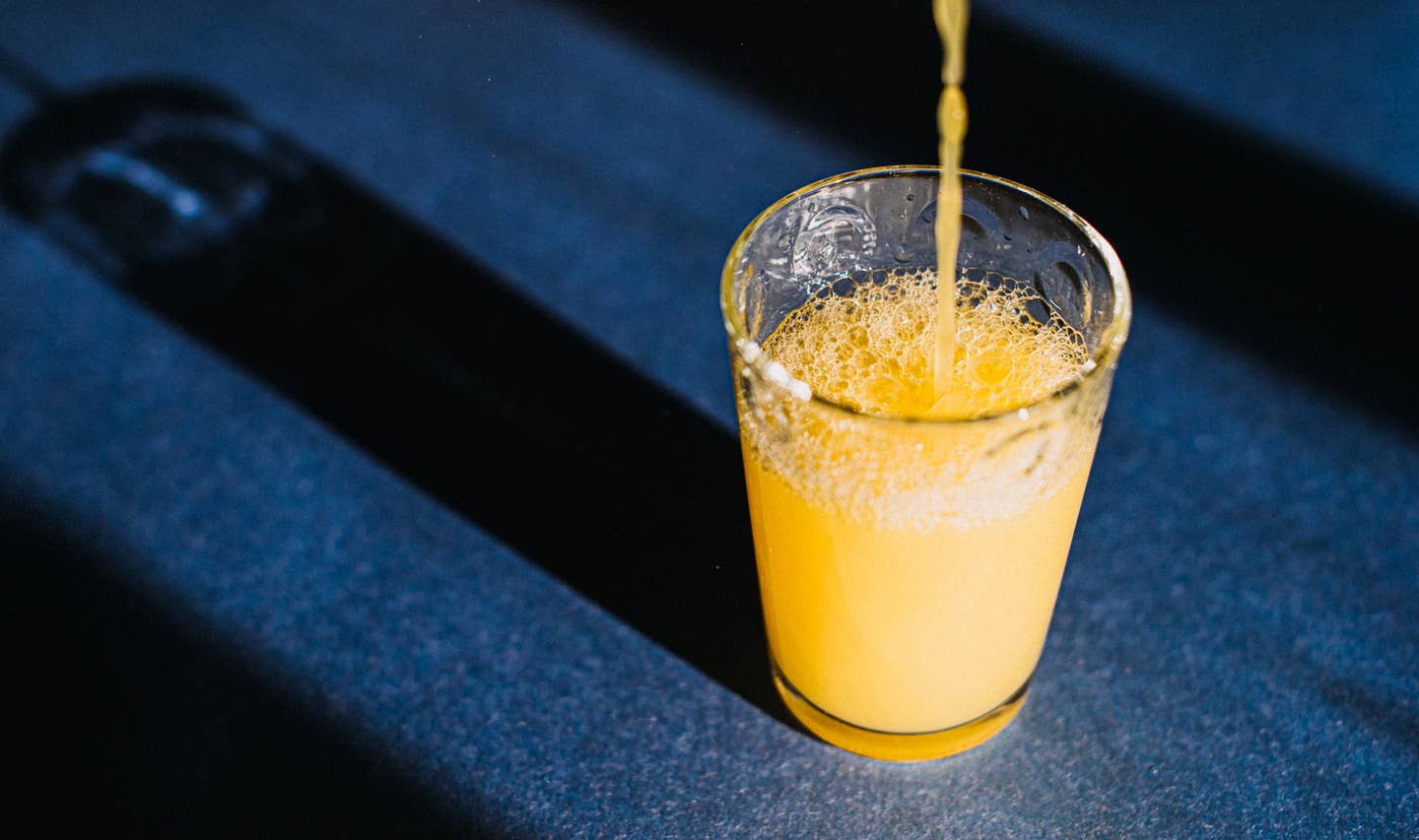 Orange Juice Being Poured in a Glass that casts a beautiful shadow on a blue surface.