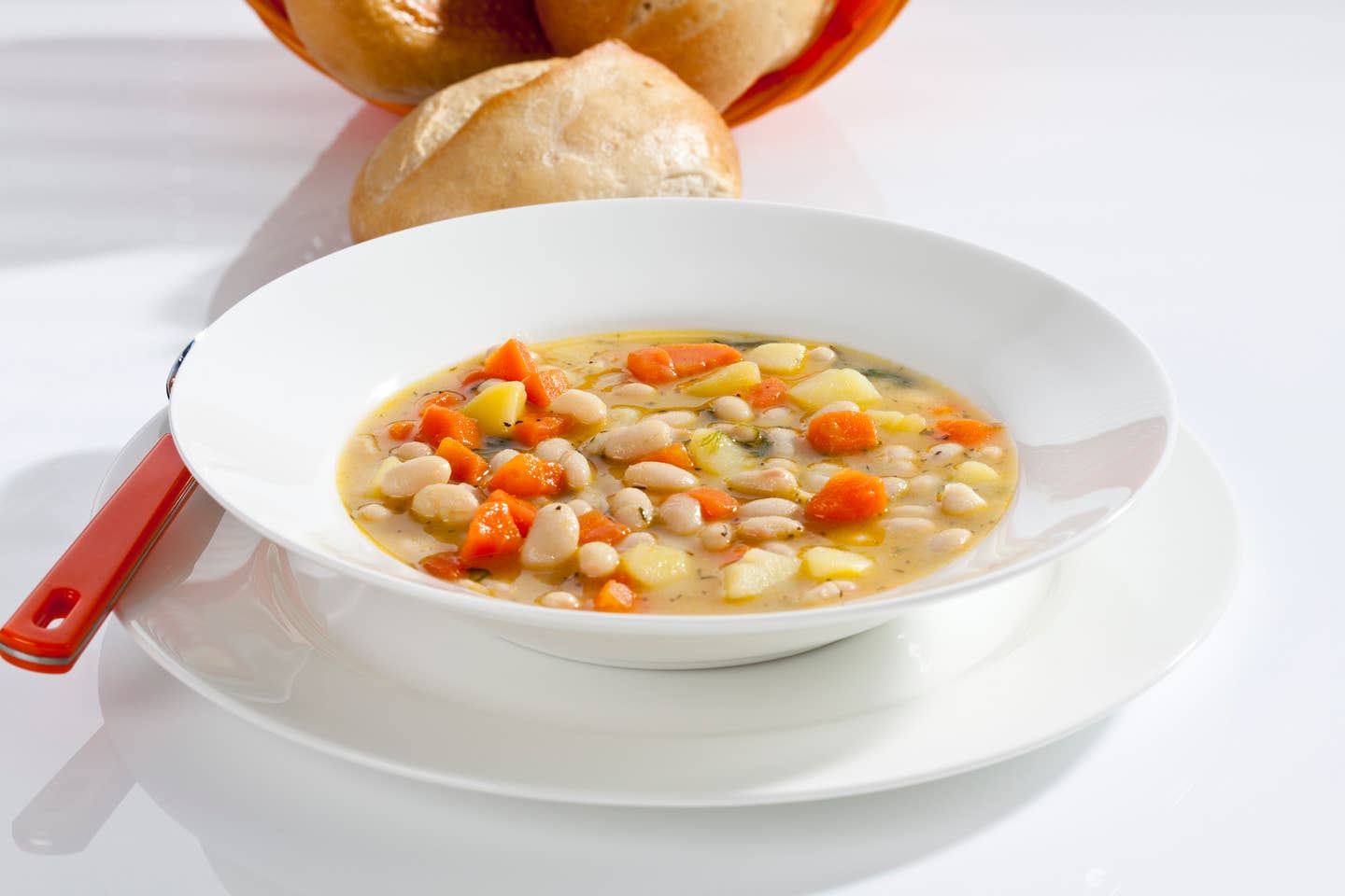 Bowl of bean soup with carrots and potatoes besides bread, close up