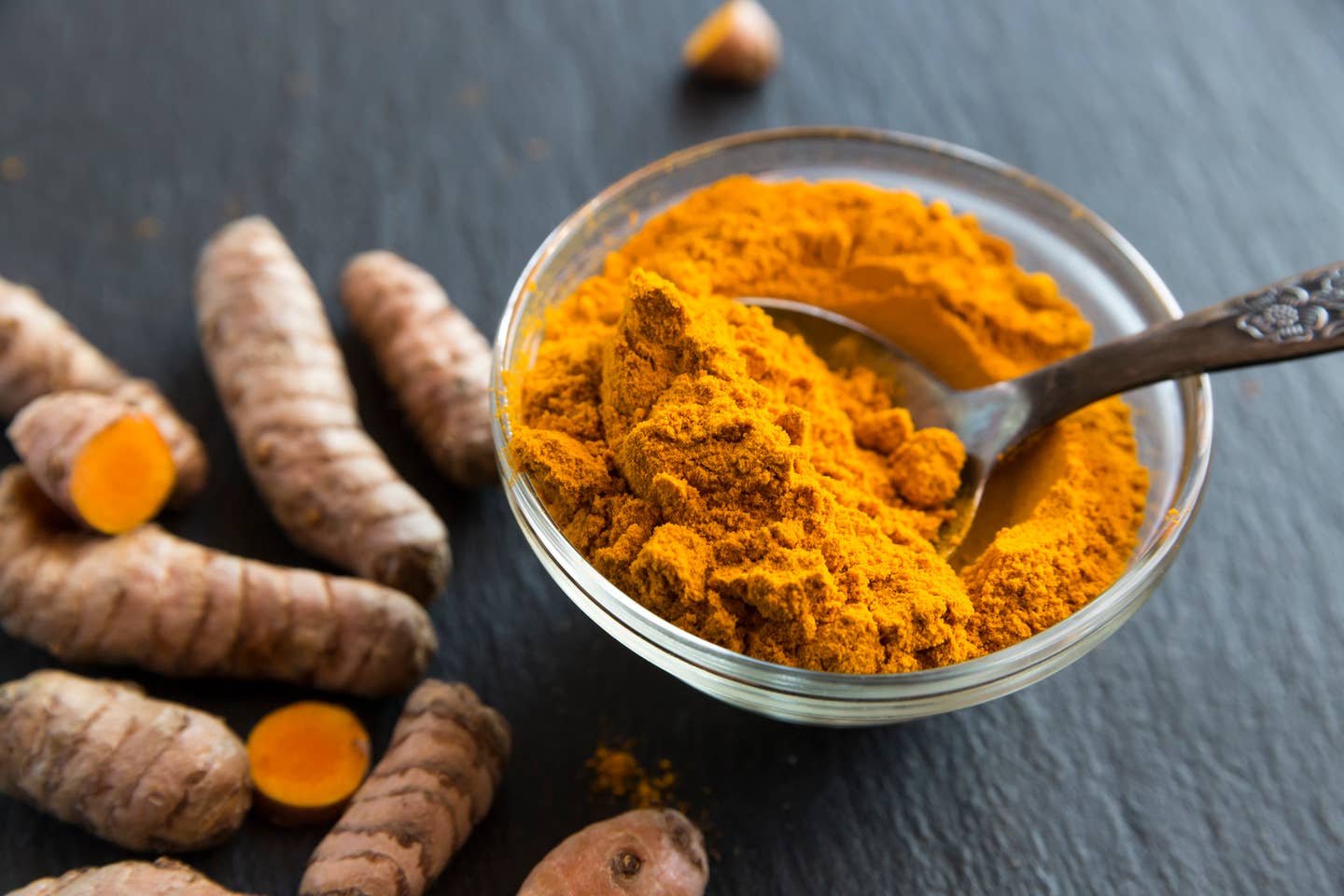 Glass bowl of curcuma powder and fresh organic curcuma on slate