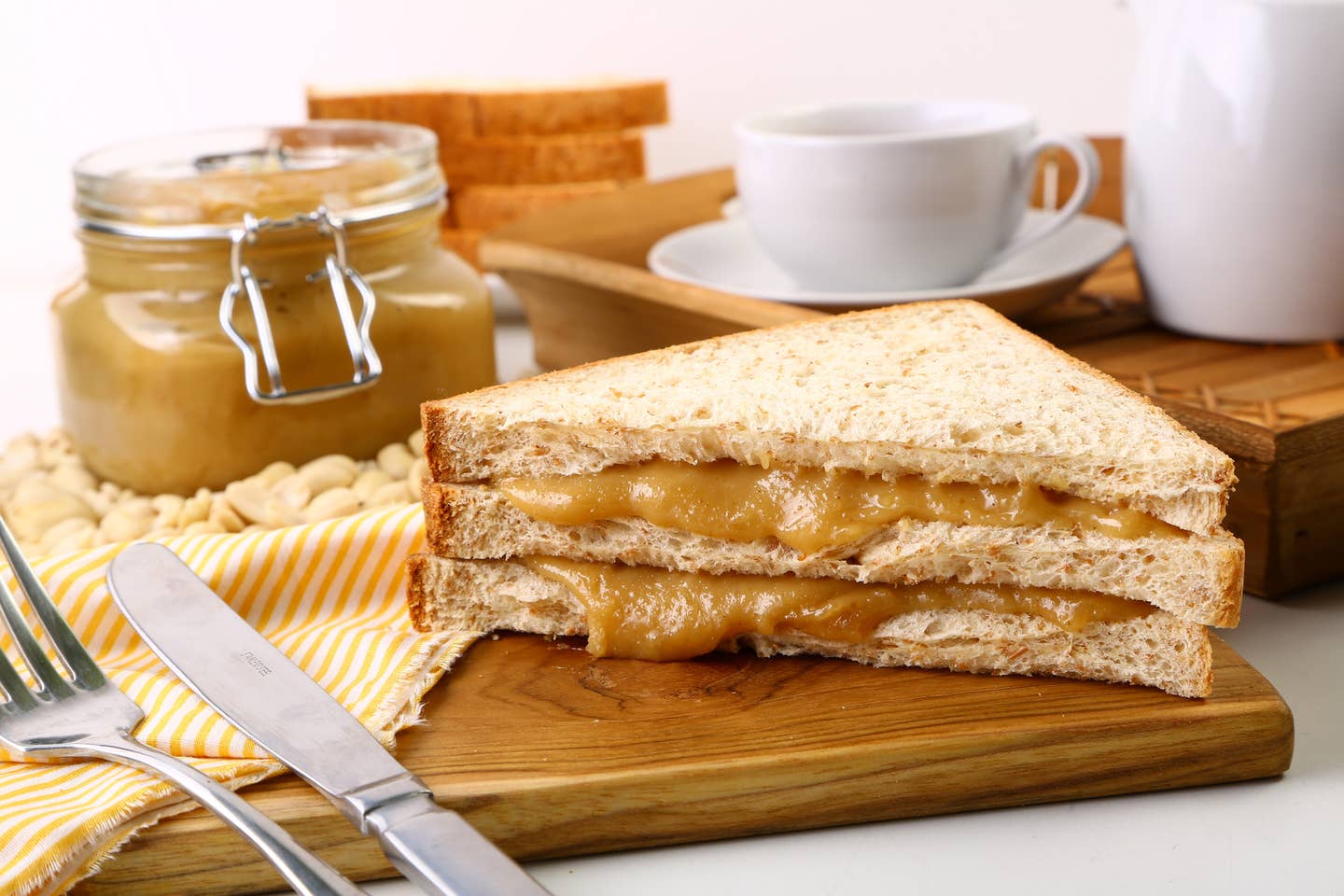 Sandwich With Tea Cup And Peanut Butter On Cutting Board Over White Background