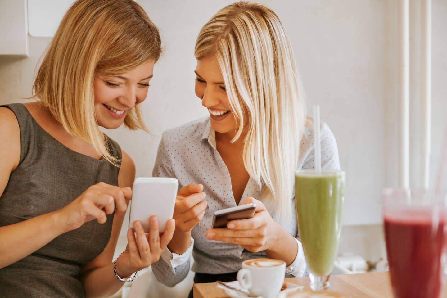 Two happy young women with smartphones in a cafe