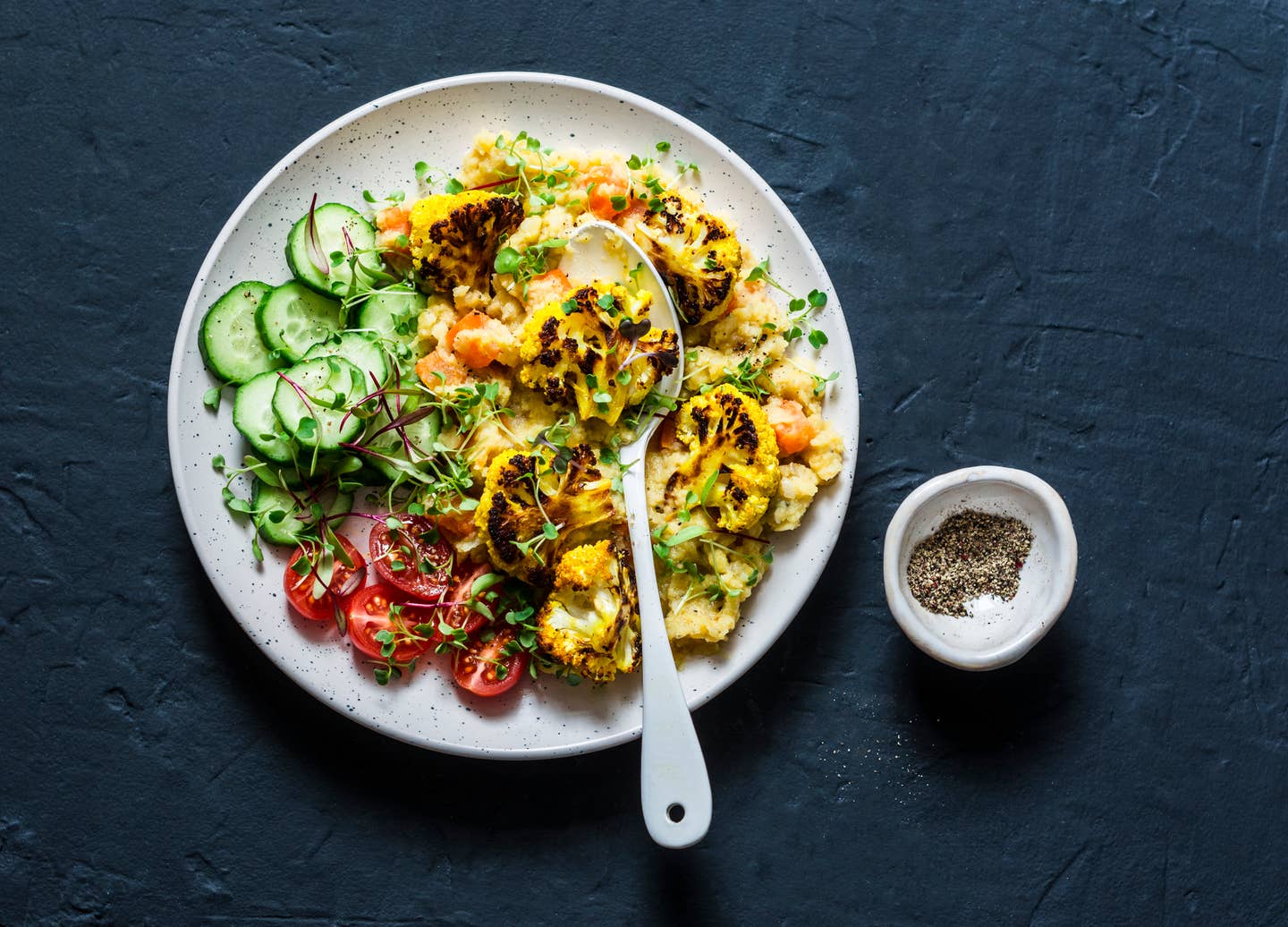 Yellow lentils, pumpkin, roasted turmeric cauliflower and vegetables in one bowl - healthy vegetarian food on a dark background, top view