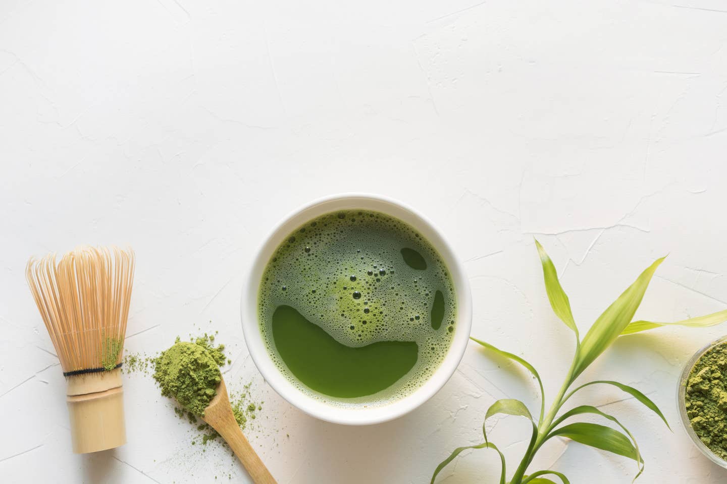 Green matcha tea and bamboo whisk on white concrete table. Top view.