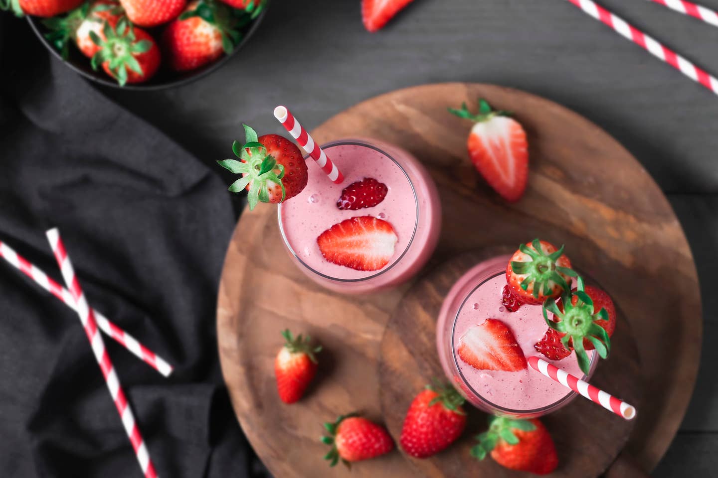 Glasses of strawberry smoothie and strawberries on dark wood