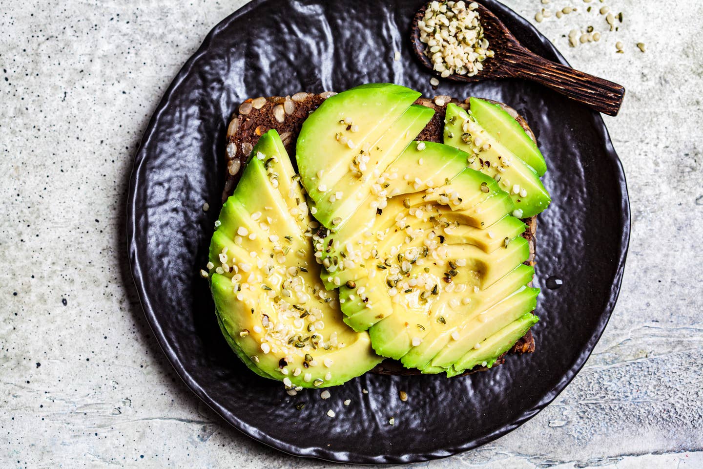 Avocado toast with rye bread and hemp seeds on black plate, top view. Healthy vegan food concept.