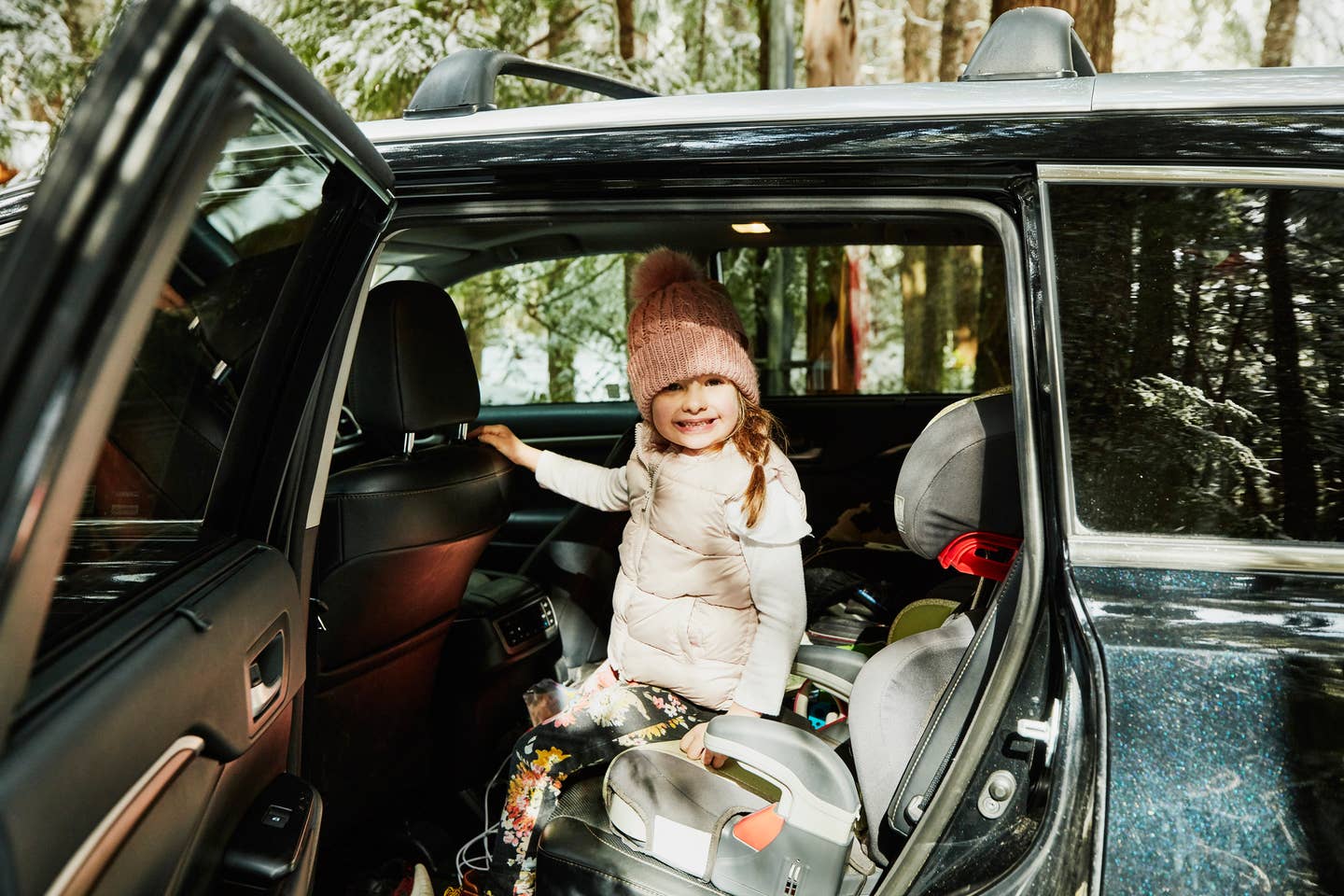 Smiling girl getting out of car after arriving at winter cabin