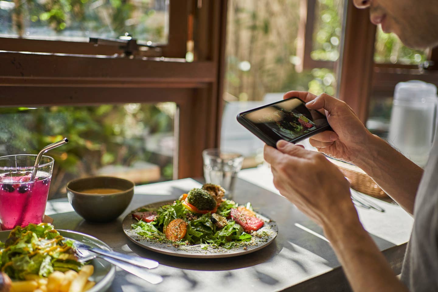 A man uses his smartphone to photograph the food he ordered at a vegan cafe.