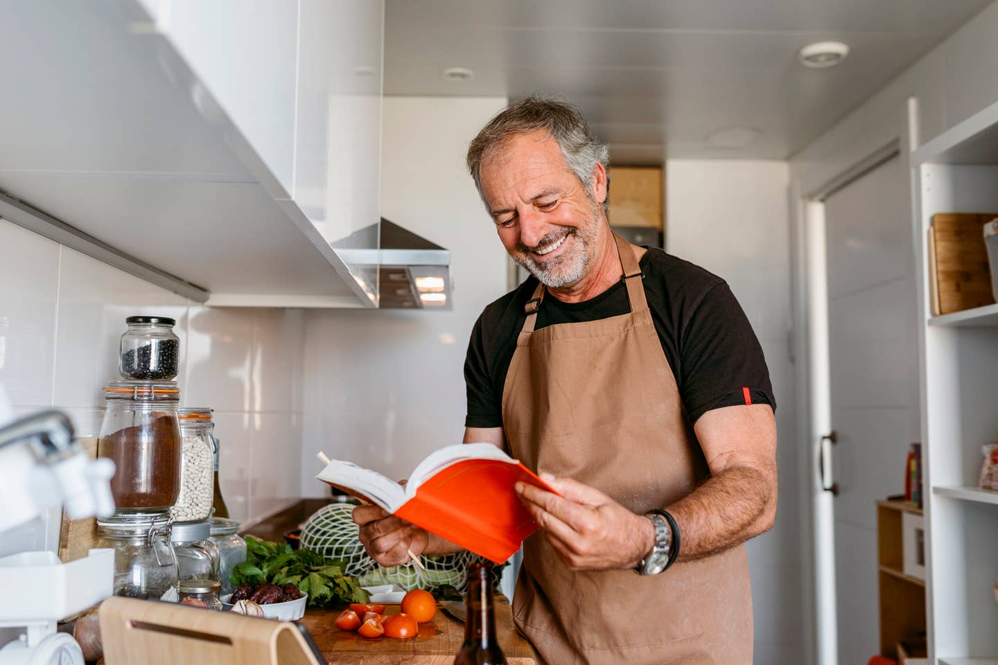 Mature man smiling while reading book in kitchen at home