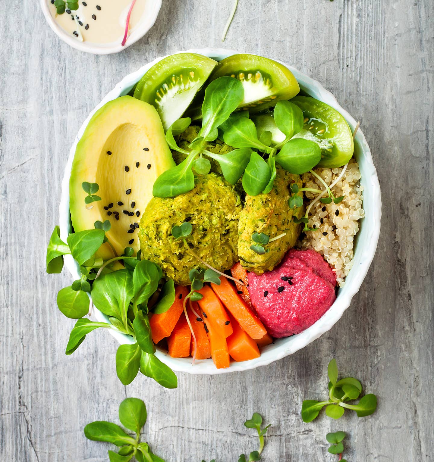 Middle eastern style Buddha bowl with green falafel, quinoa, butternut squash, tomatoes, avocado, beetroot hummus, micro greens and tahini sauce.